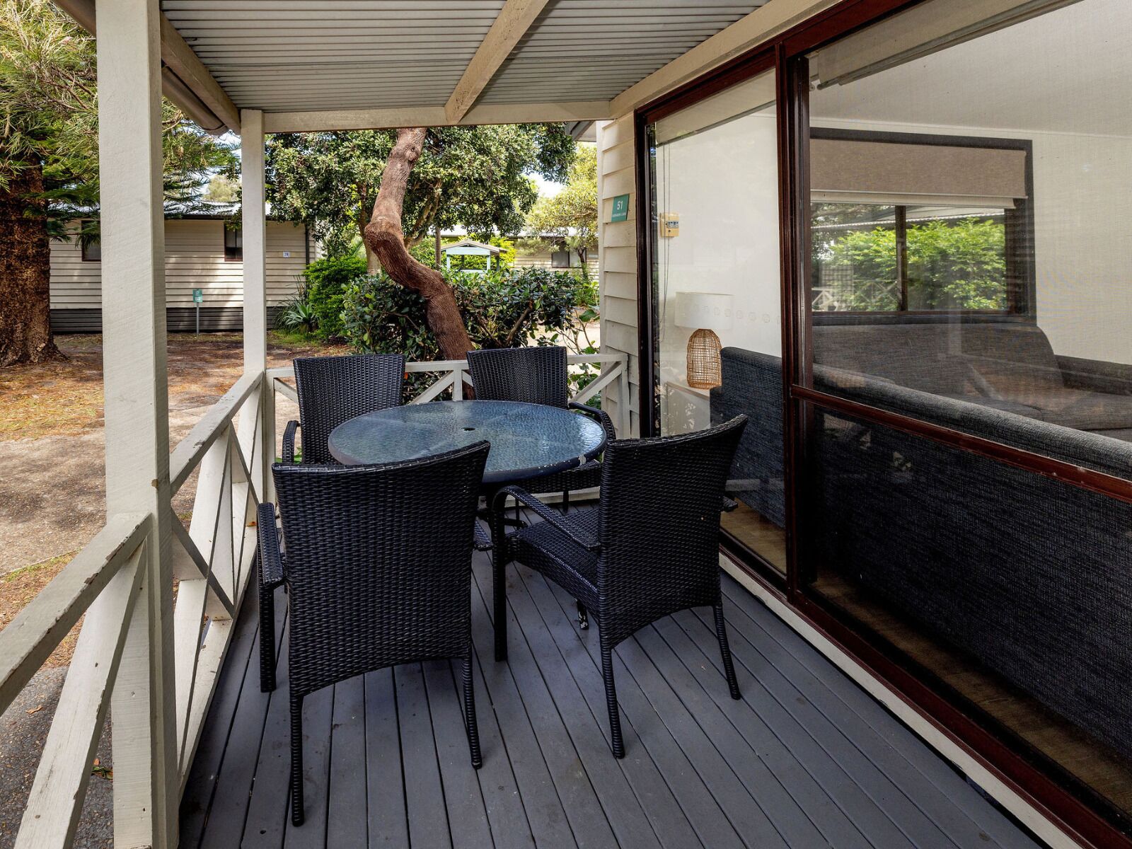 A covered outdoor seating area with a table and chairs, a view of the surrounding greenery, and a building with a large window.