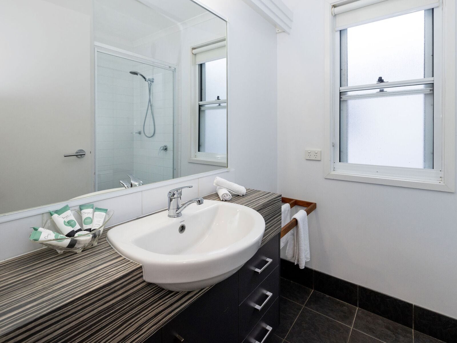 A modern bathroom with a white sink, a large mirror, and a shower.