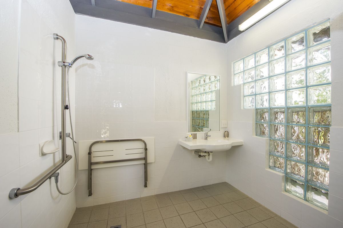 A bathroom with a shower, a sink, a mirror, and a window with frosted glass.
