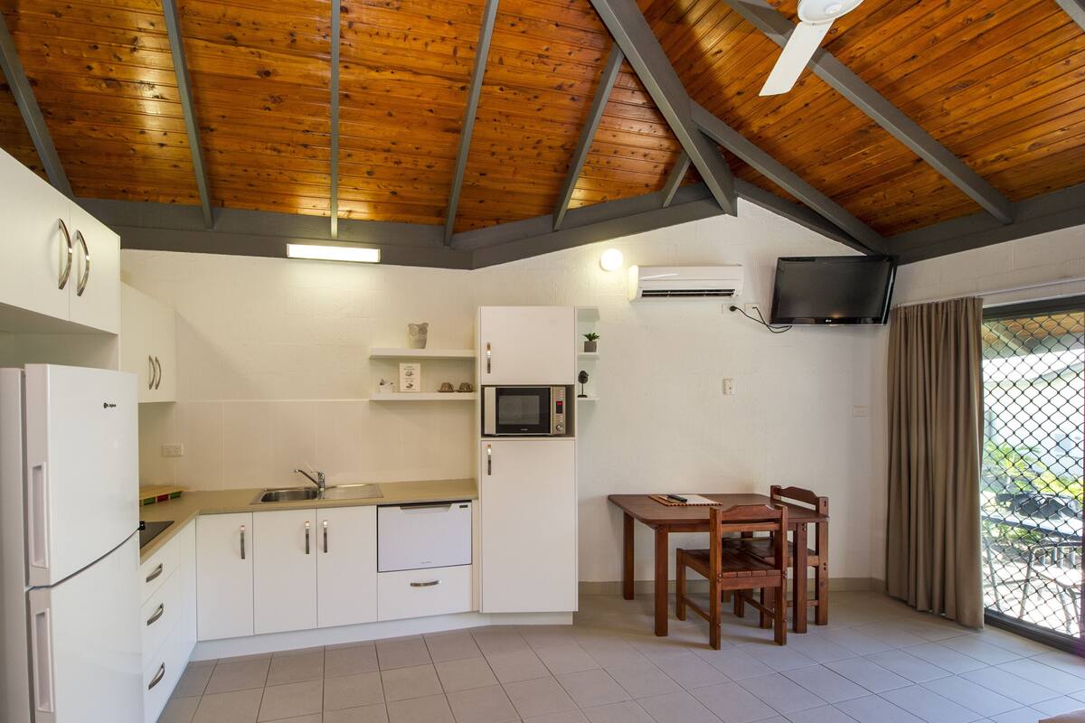 A compact kitchen with white cabinets, a microwave, and a dining area with a table and chairs.