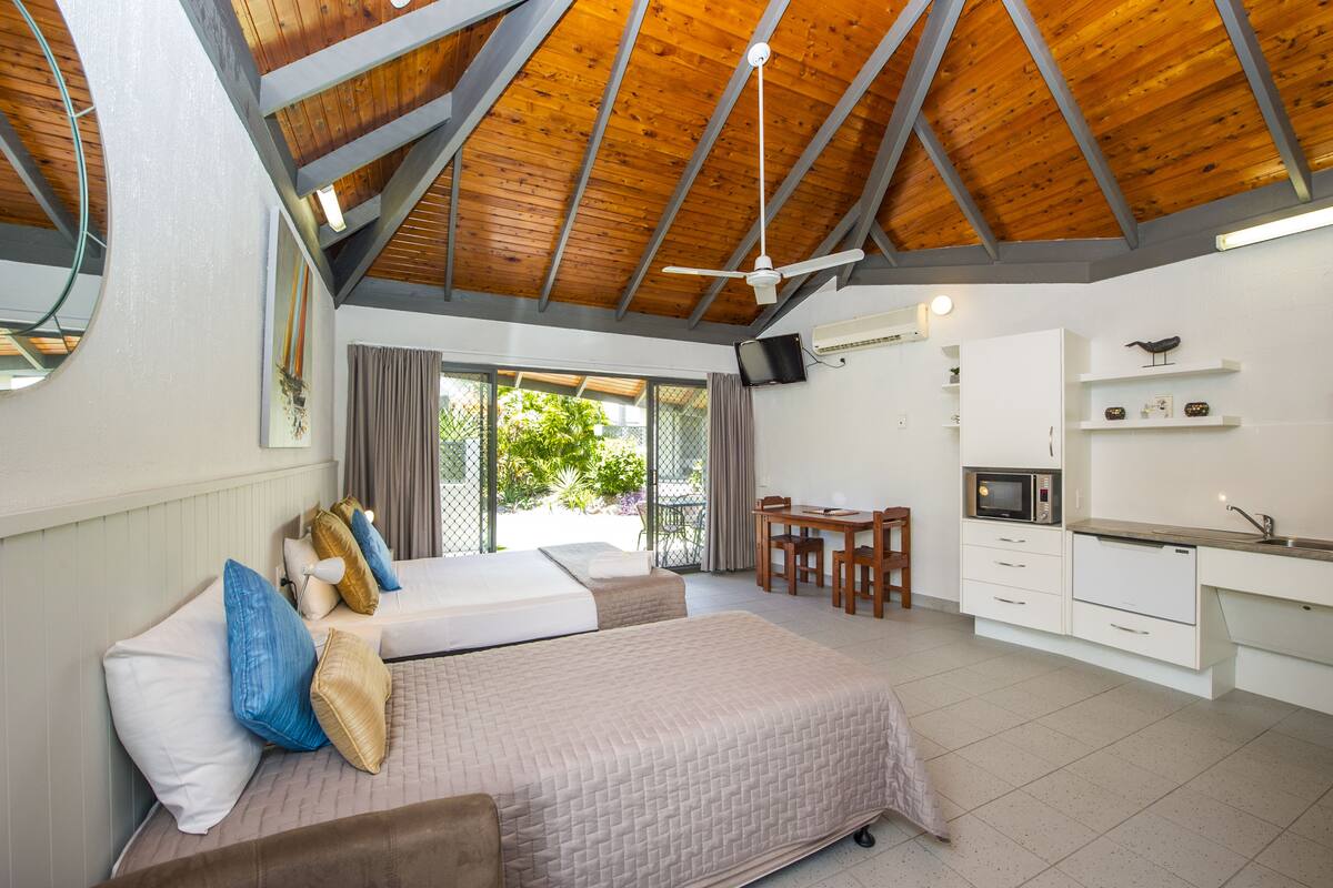 A bedroom with two beds, a desk, a TV, and a kitchenette.