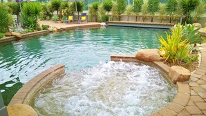 Ein Swimmingpool mit Wasserspiel in der Mitte, umgeben von Palmen und Liegestühlen.