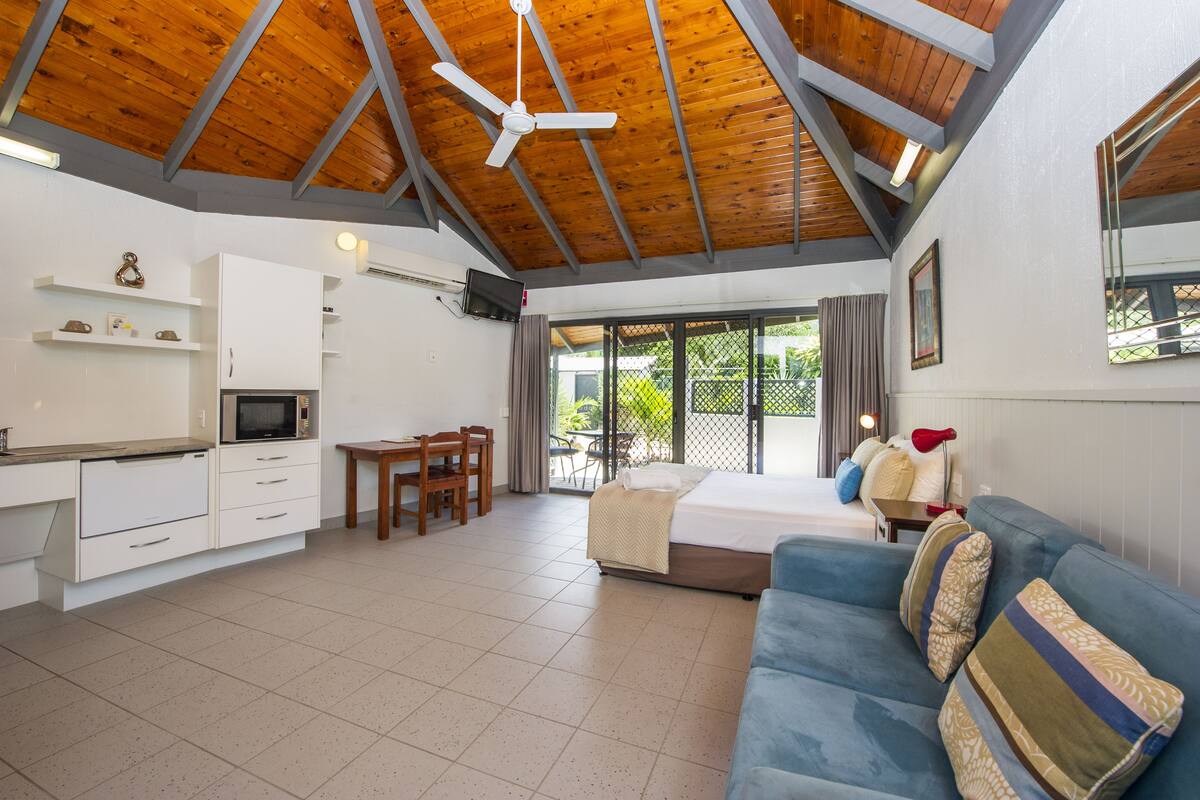 A spacious room with a wooden ceiling, a kitchenette, a dining area, a large bed, and a blue sofa.