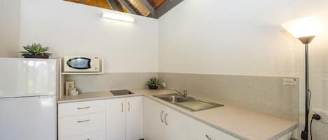 A kitchen with white cabinets, a microwave, a sink, and a ceiling fan.