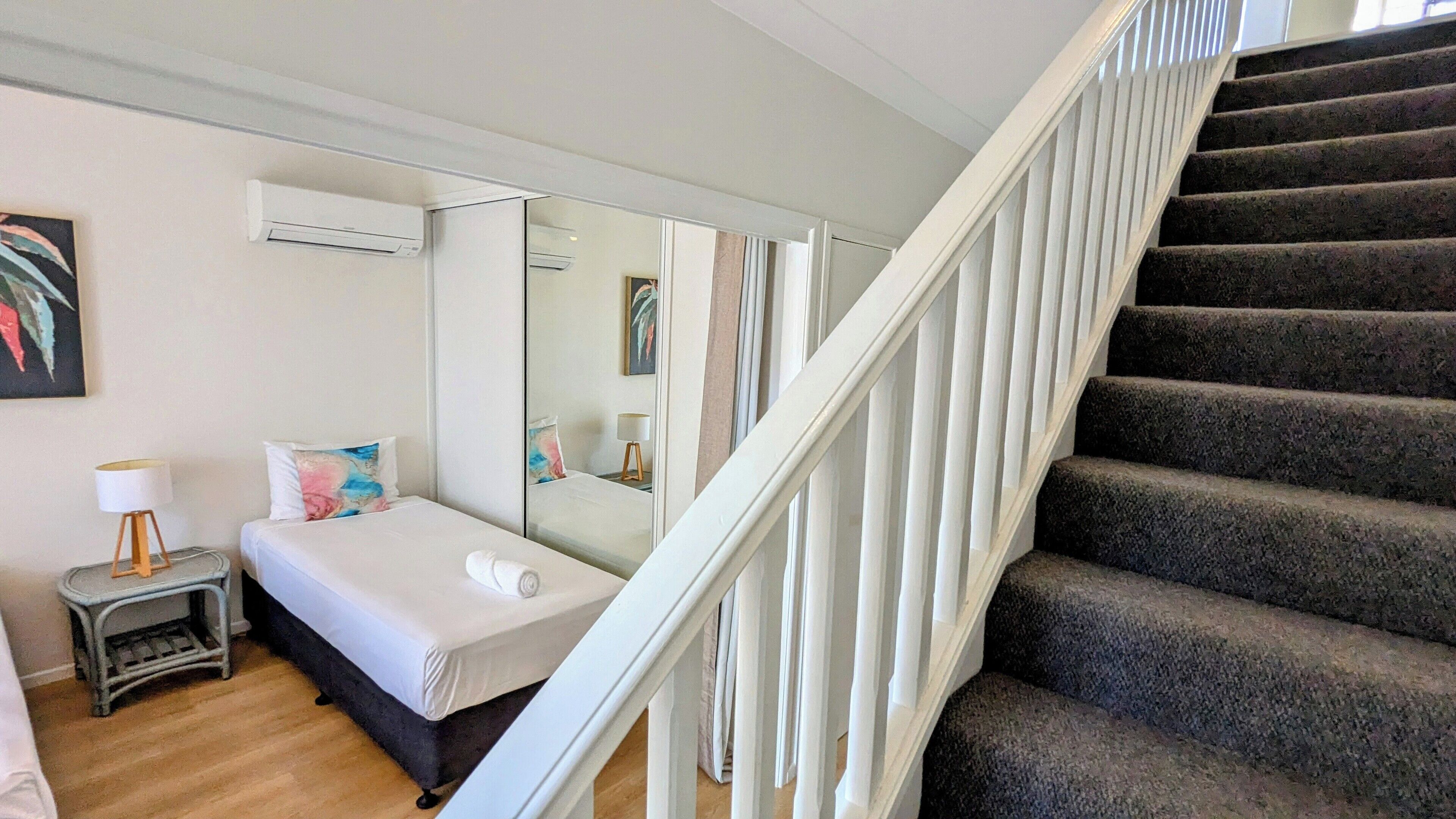 Une chambre d’hôtel avec un lit, une table de chevet, une lampe, un miroir et un escalier.