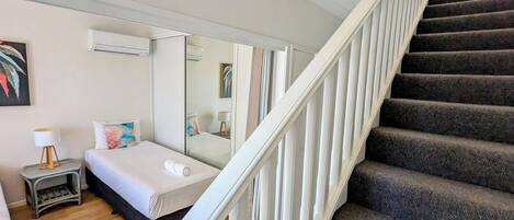 Une chambre d’hôtel avec un lit, une table de chevet, une lampe, un miroir et un escalier.