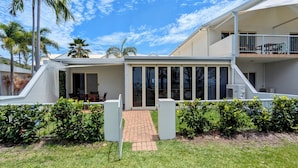 A modern two-story building with a covered patio area, a brick pathway leading to the entrance, and a fenced garden. - Sails On Horseshoe (Horseshoe Bay)