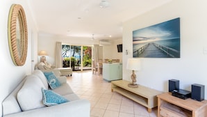 A modern living room with a sofa, a coffee table, and a painting of a pier. There is a dining area with a table and chairs visible in the background. - Sails On Horseshoe (Horseshoe Bay)