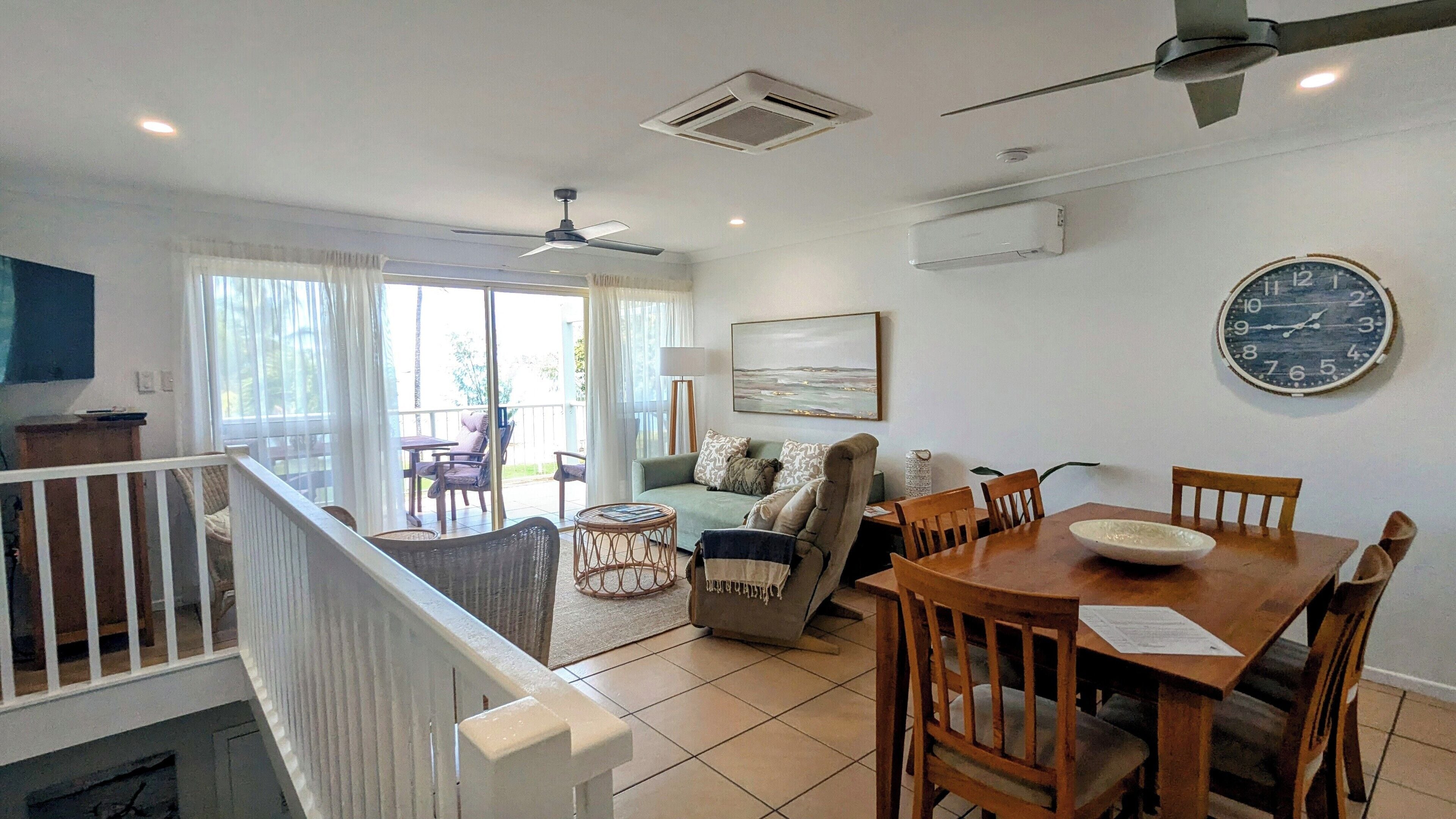 A spacious living area with a dining table, chairs, a sofa, and a balcony with outdoor furniture.