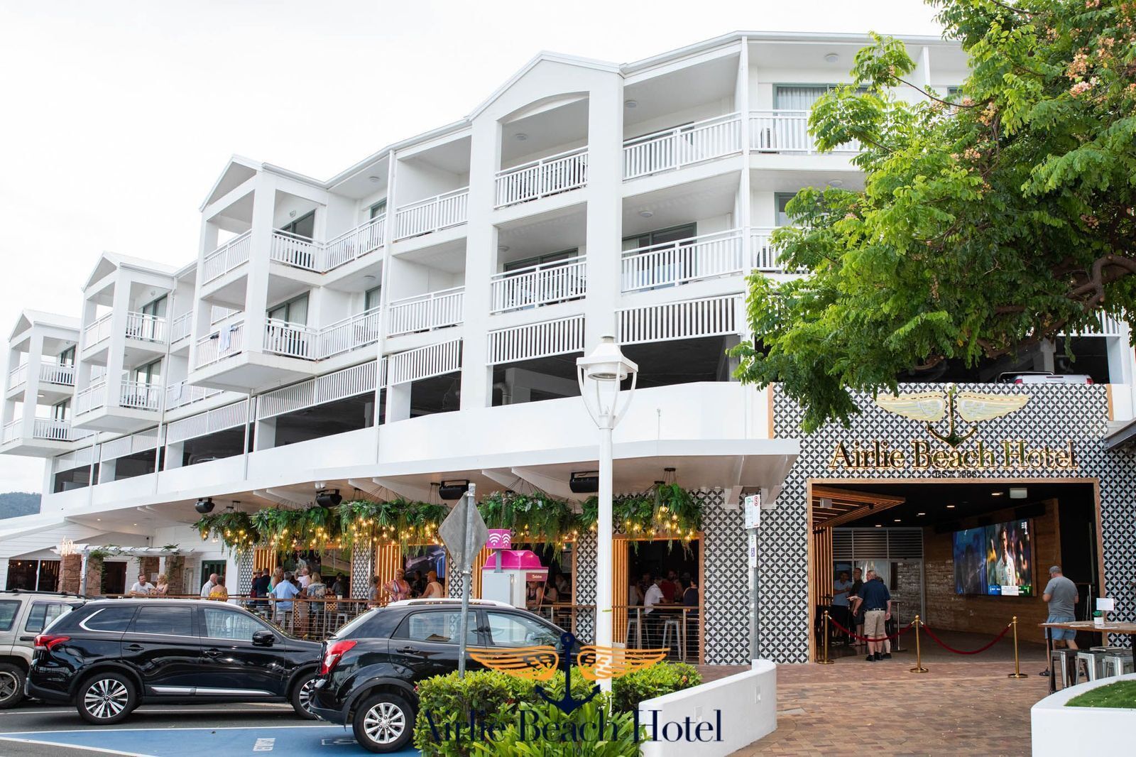 A multi-story hotel with a white facade, outdoor seating area, and a visible entrance.