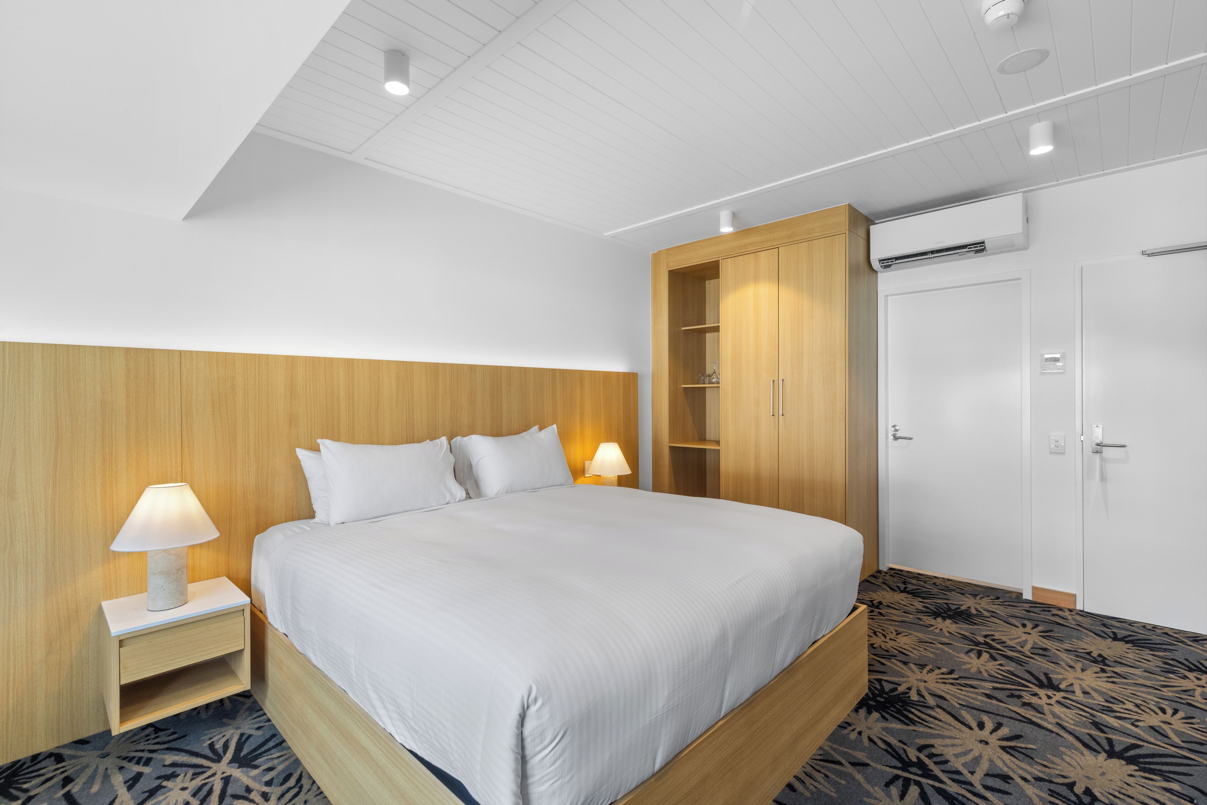 Habitación de hotel con cama, mesitas de noche, armario y aire acondicionado.