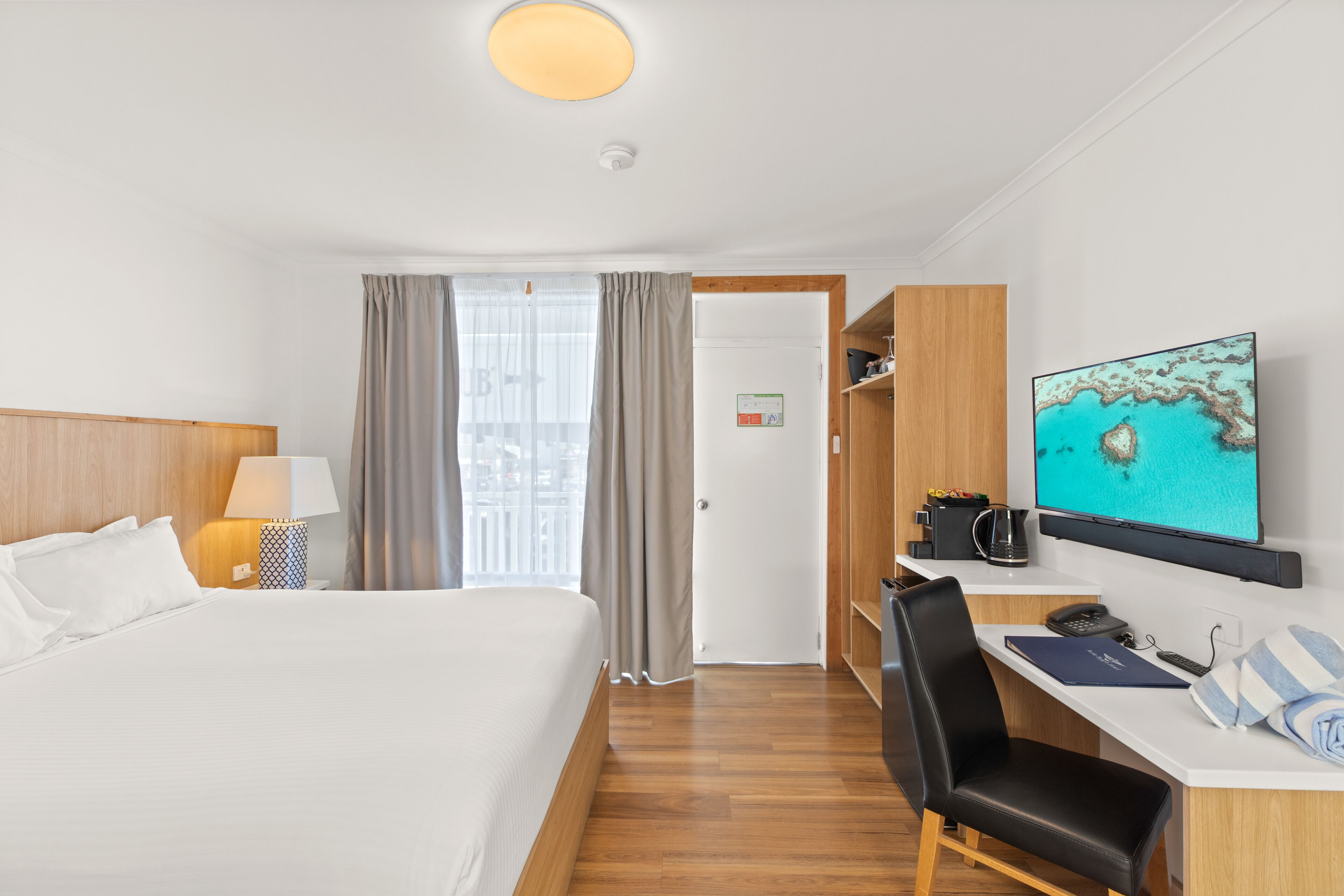 A hotel room with a bed, desk, chair, TV, and a view of the city through the window.