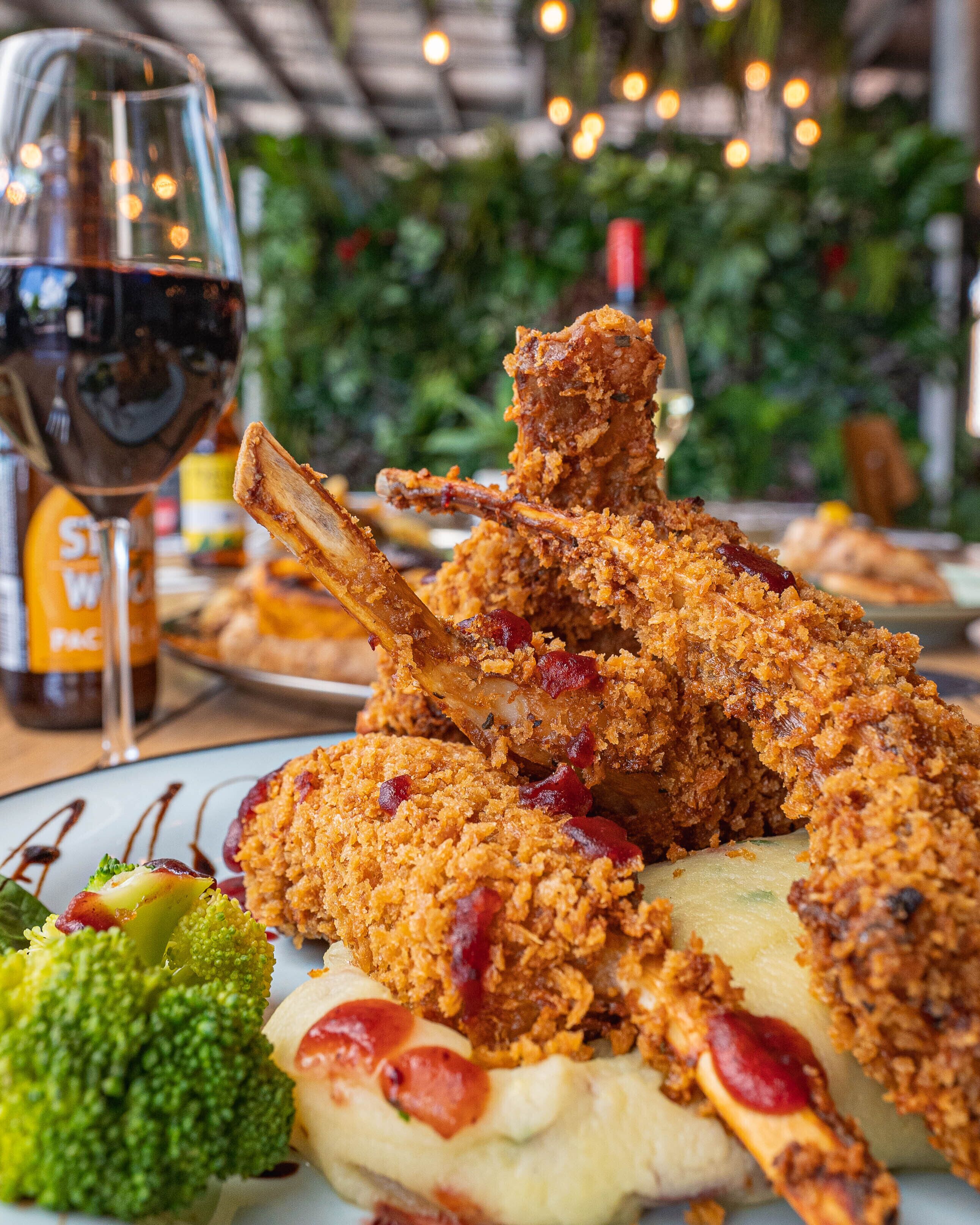 A plate of fried chicken with mashed potatoes and broccoli, accompanied by a glass of red wine.