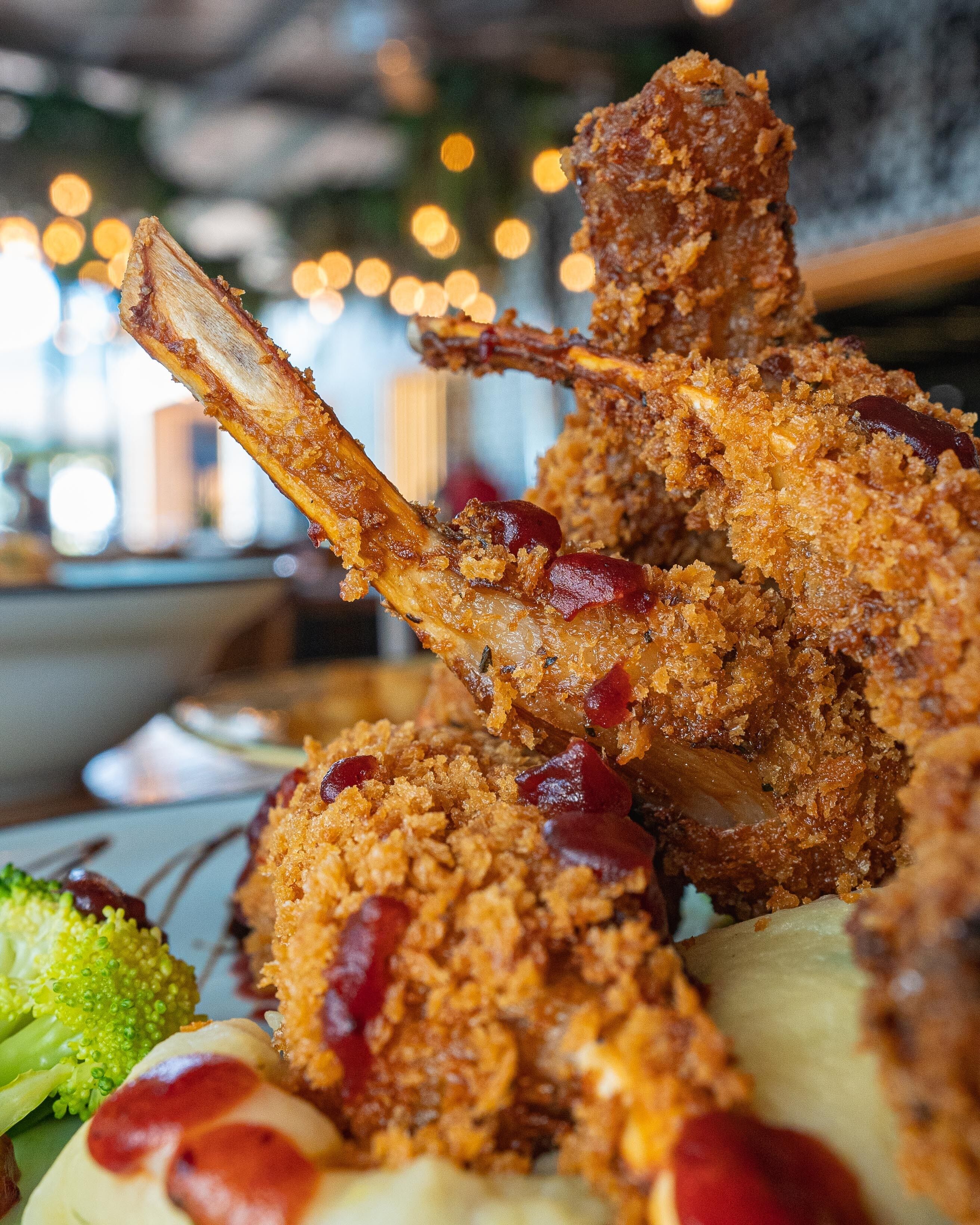 A close-up of a crispy fried chicken leg with a golden-brown coating, served alongside a green vegetable and a creamy sauce.