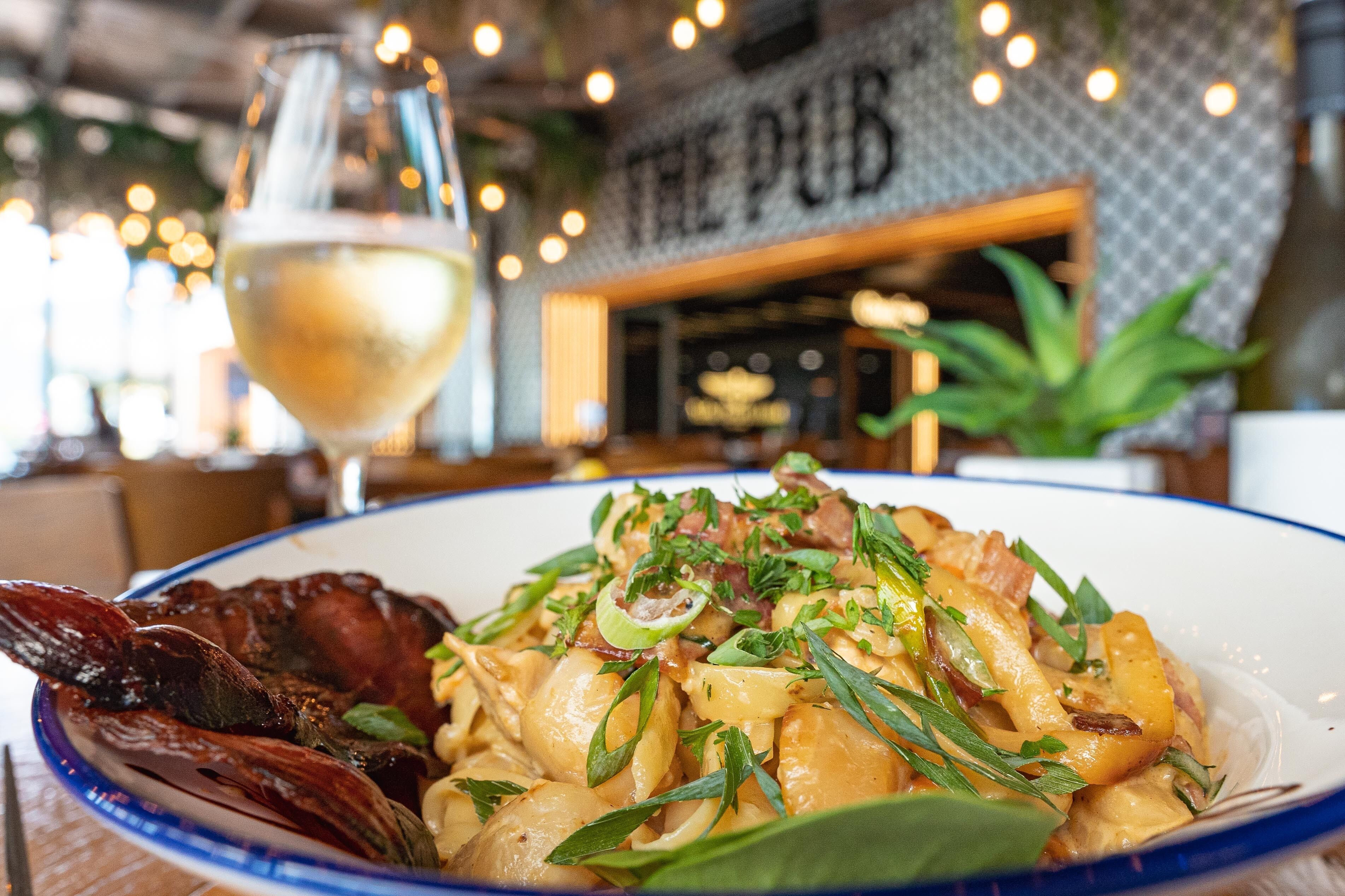 A plate of pasta with a glass of white wine on a table in a restaurant.