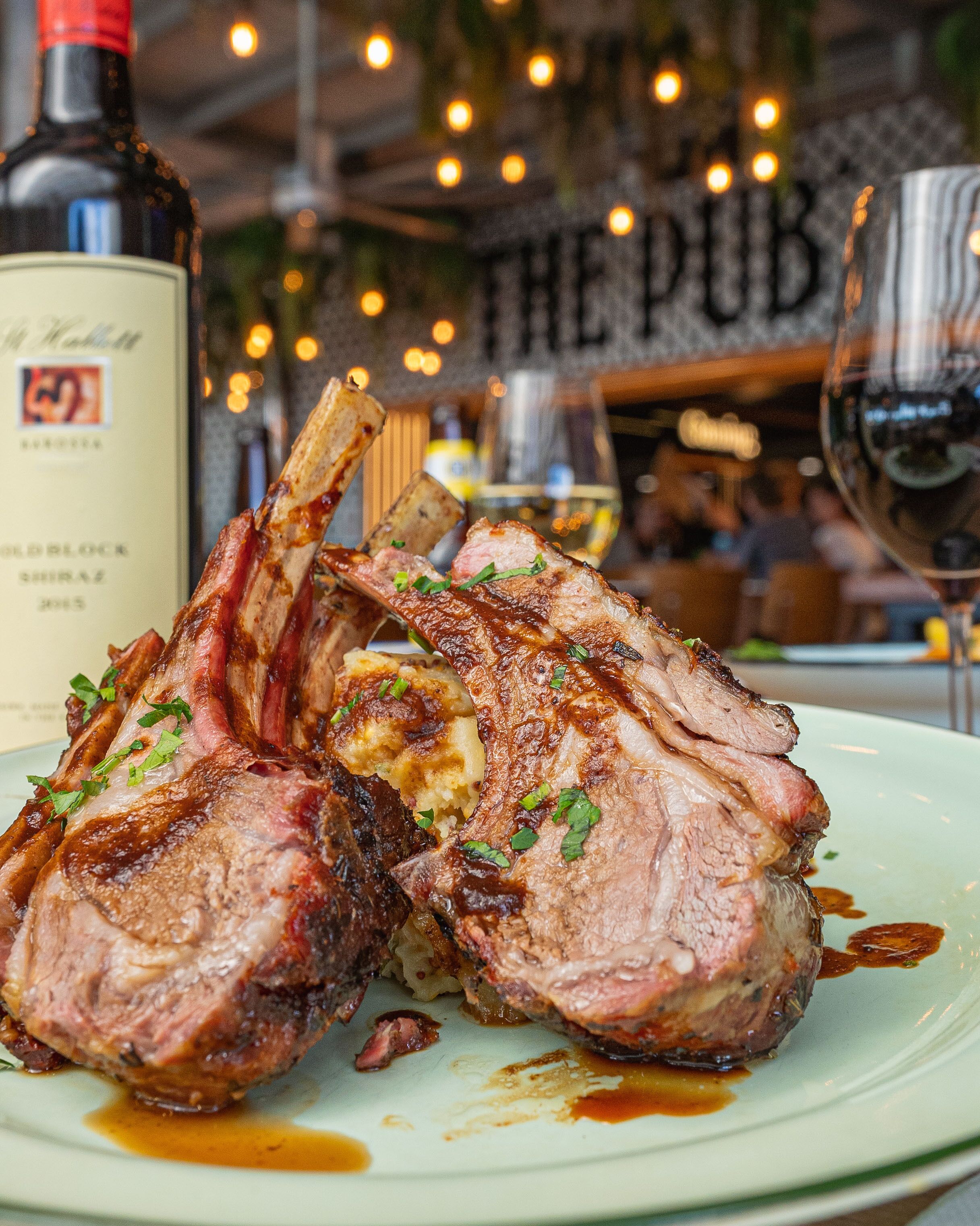 Un piatto di costolette di agnello cotte con salsa, una bottiglia di vino e un bicchiere di vino su un tavolo in un ristorante.