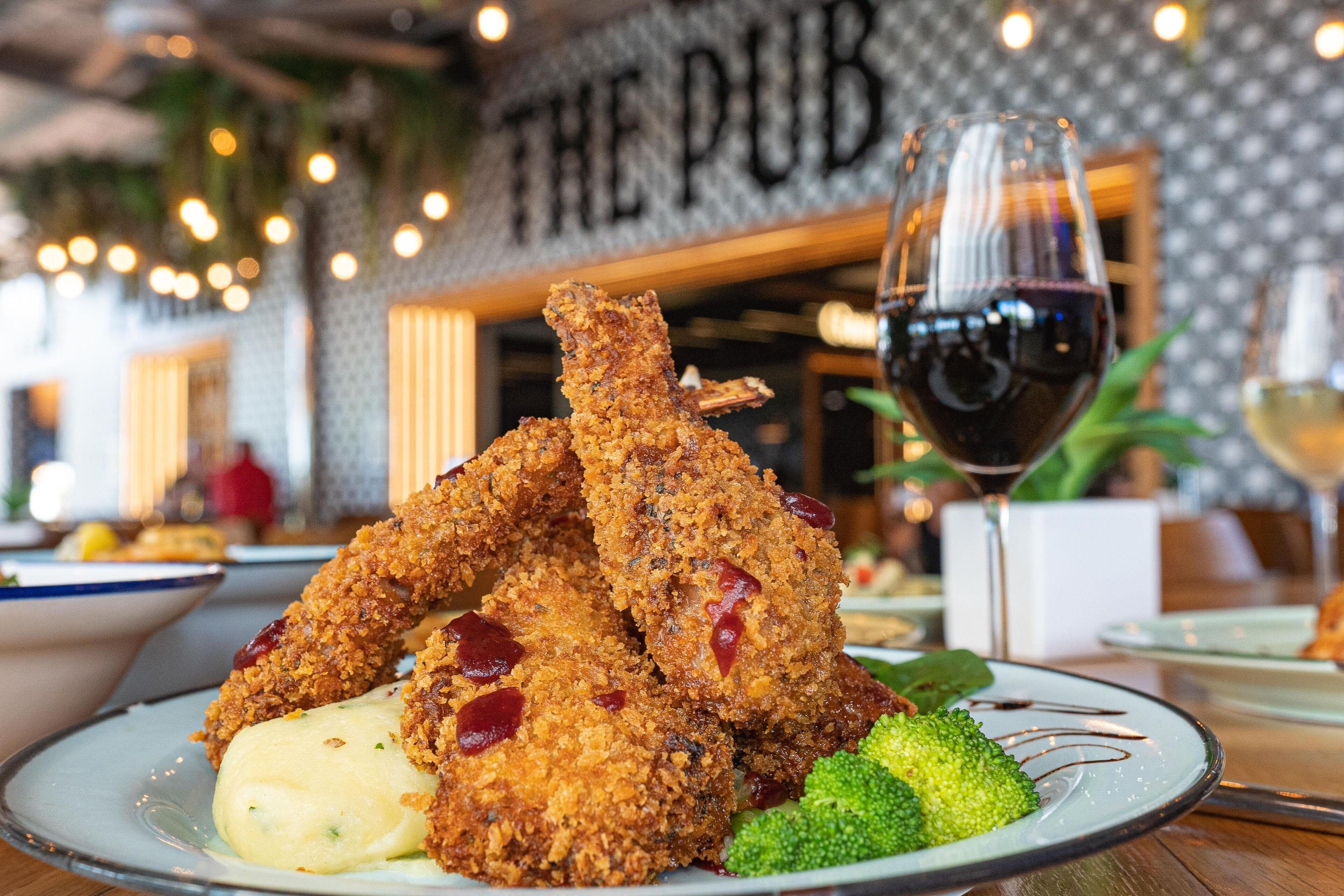 A plate of fried chicken with sauce, broccoli, and a glass of red wine.