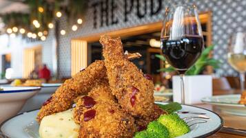 A plate of fried chicken with sauce, broccoli, and a glass of red wine.