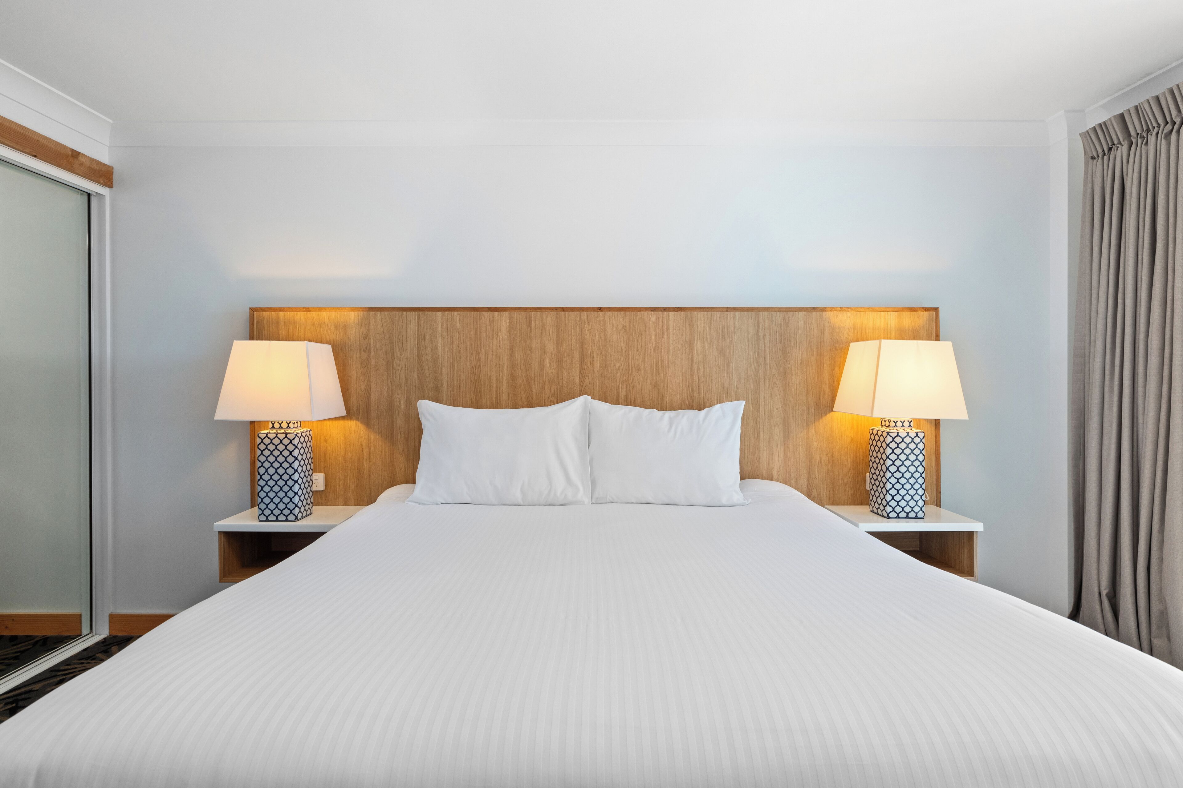 A neatly made bed with white linens, two bedside lamps with patterned bases, and a wooden headboard.