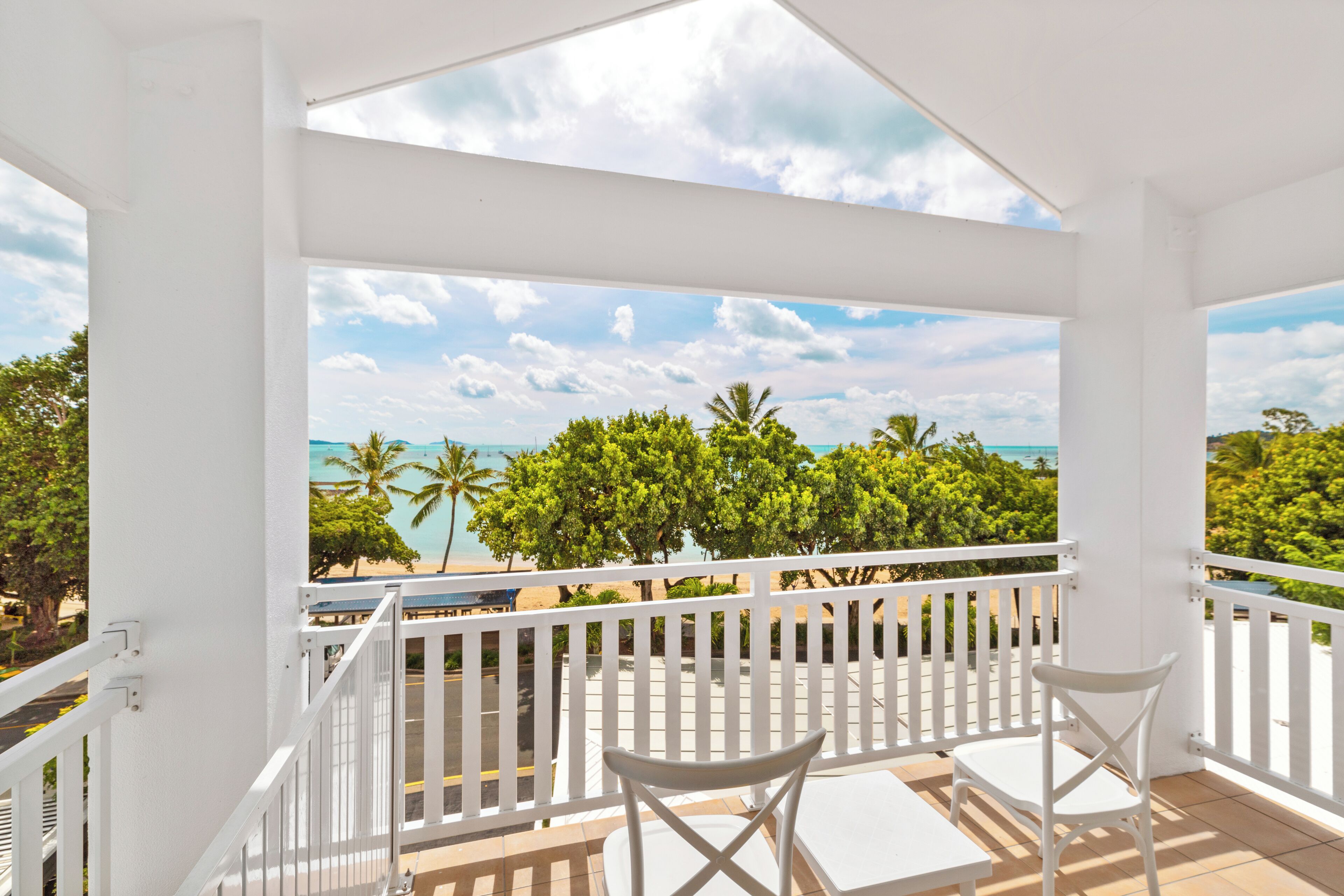 A balcony with white railings, two white chairs, and a view of the beach and ocean.