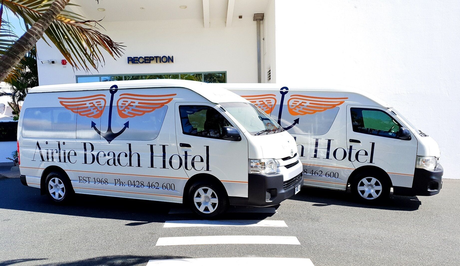 Two white vans with 'Airlie Beach Hotel' branding, parked in front of a building with a 'RECEPTION' sign.