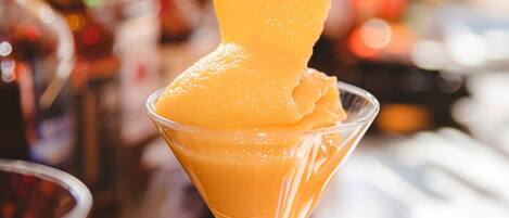 Una copa de martini de vidrio transparente llena de un postre espeso de color naranja, probablemente un sorbete de mango o algo parecido, con una cuchara dentro.