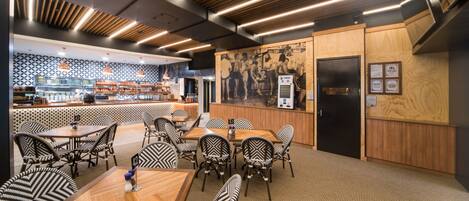 A restaurant with a modern interior, featuring wooden tables and chairs, a patterned wall, and a kitchen area visible in the background.