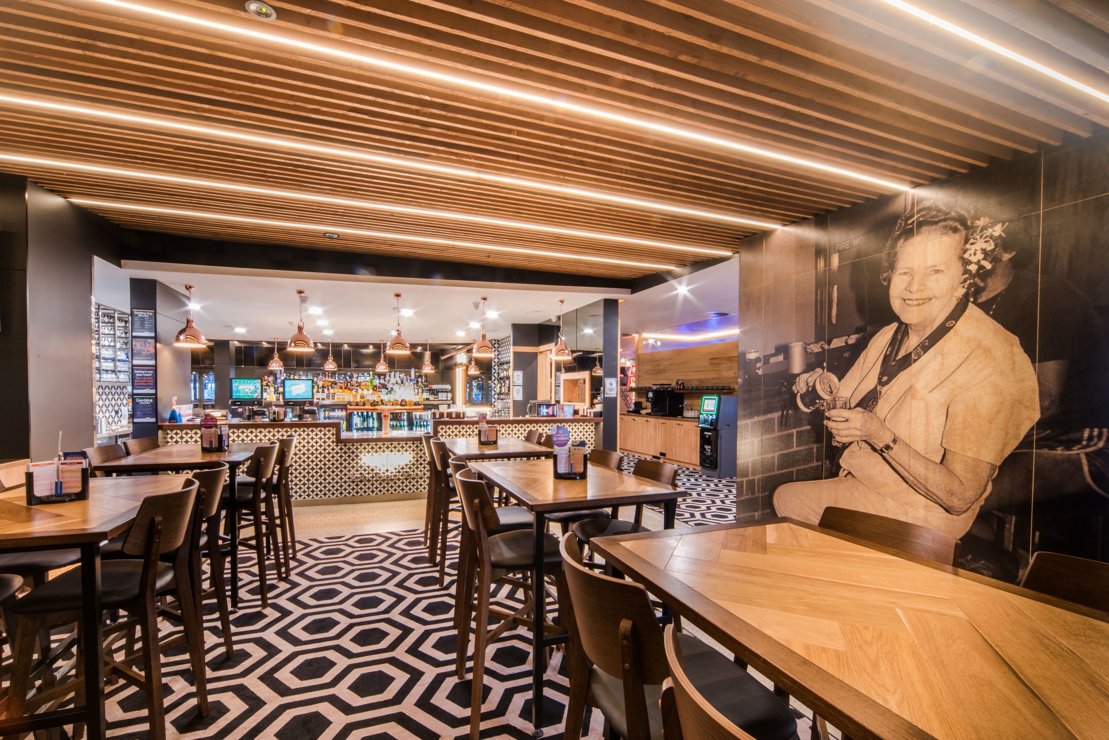 A modern bar area with wooden ceiling, bar stools, and a patterned floor.