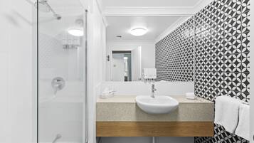 A modern bathroom with a glass shower enclosure, a sink with a wooden countertop, and patterned wallpaper.
