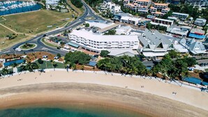 Vista aérea de una zona costera con playa, puerto deportivo y un moderno complejo de edificios de varios pisos y techo plano.