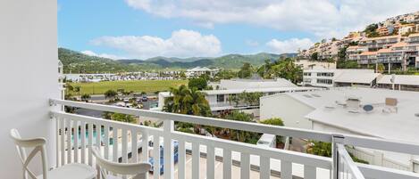 A balcony with white railings overlooking a residential area with houses and a swimming pool.