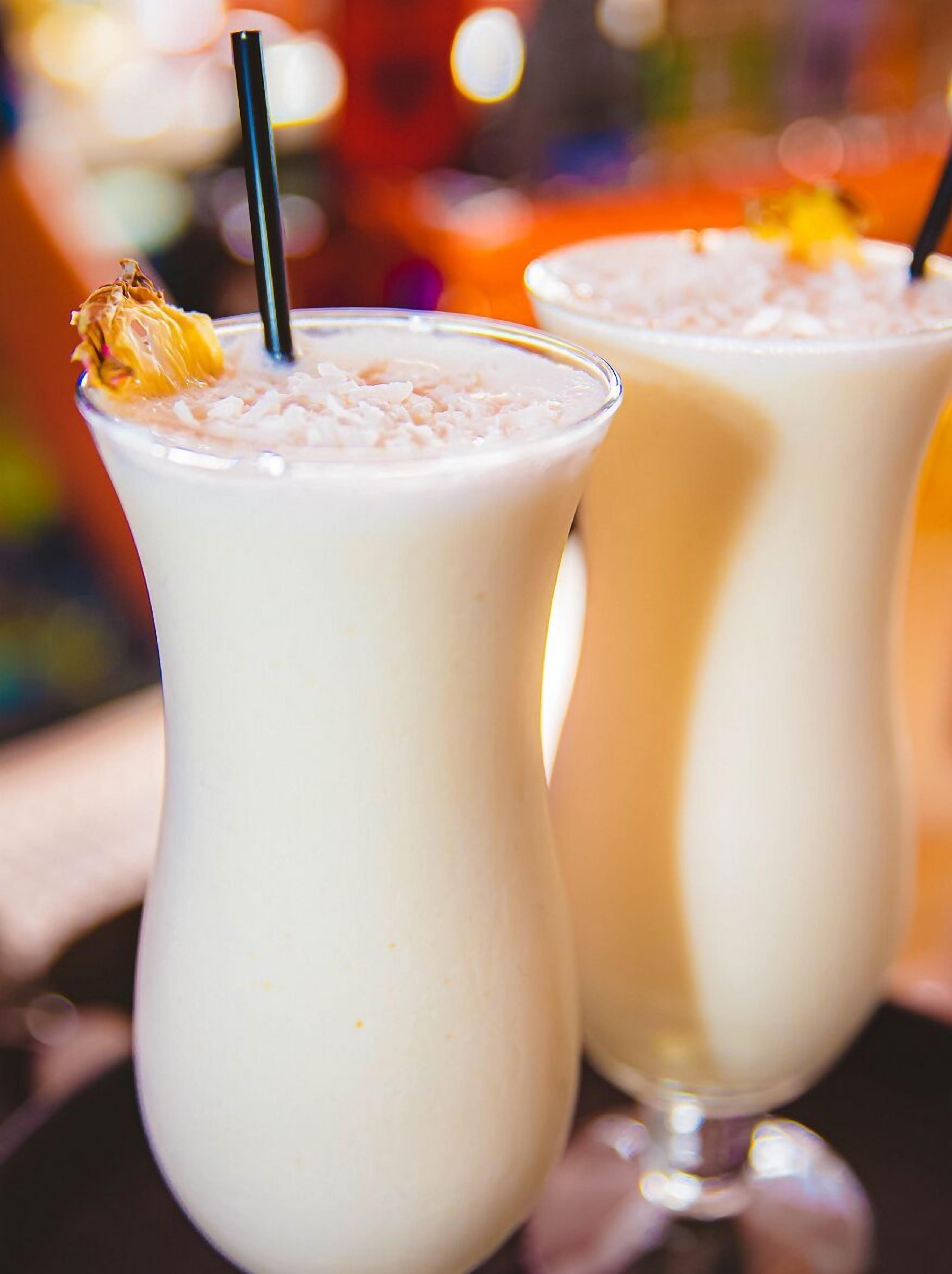 Two tall glasses of a creamy beverage with a straw and a garnish, possibly a dessert drink, on a reflective surface.