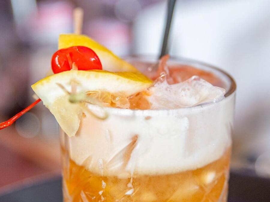 A glass with a layered beverage, ice, and garnishes.