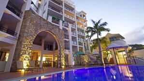 Un hotel de varios pisos con piscina, arco de piedra y zona de estar al aire libre.