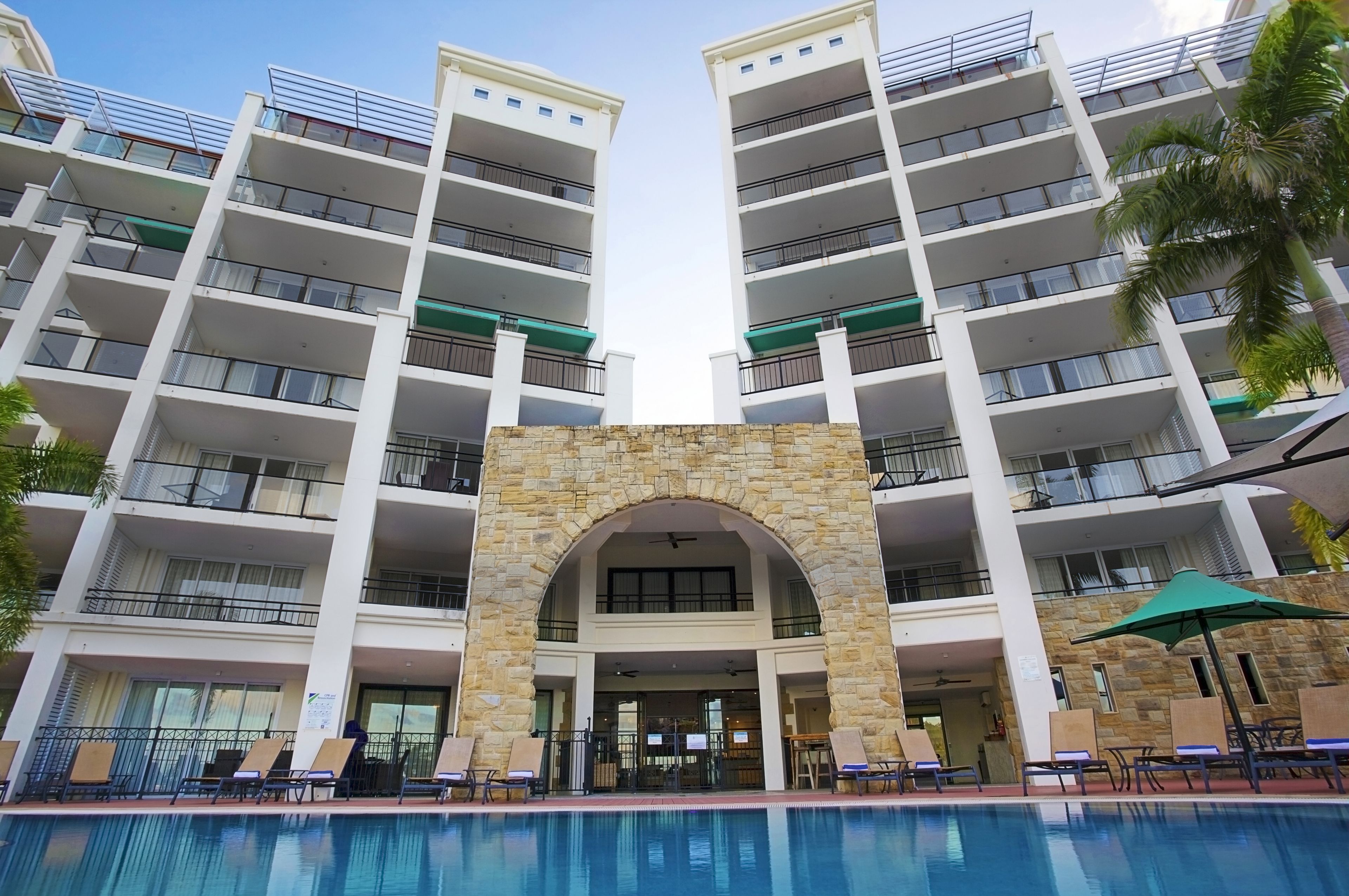A multi-story hotel with a central entrance, balconies, and a pool area.