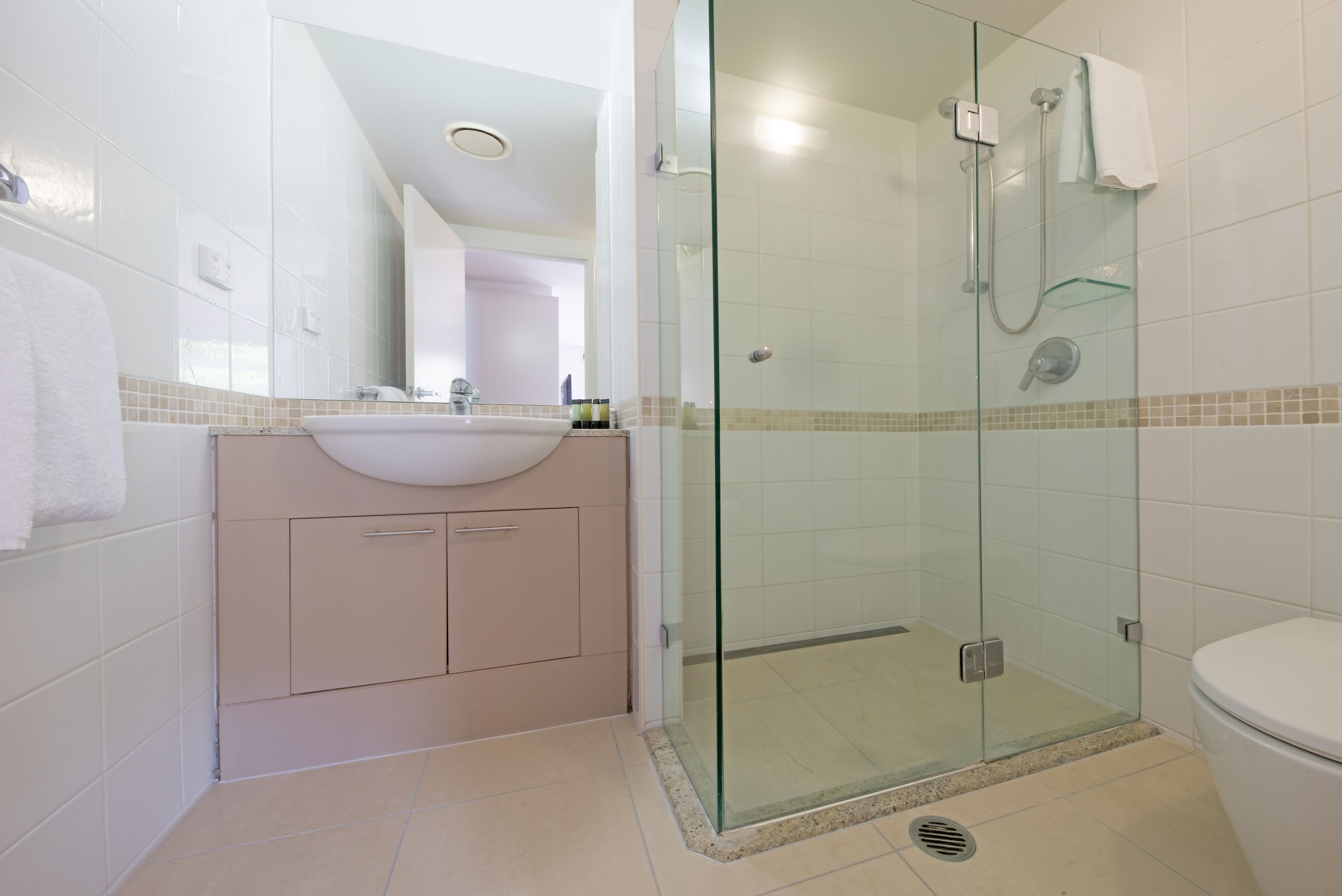 A modern bathroom with a glass-enclosed shower, a white sink, and beige cabinets.
