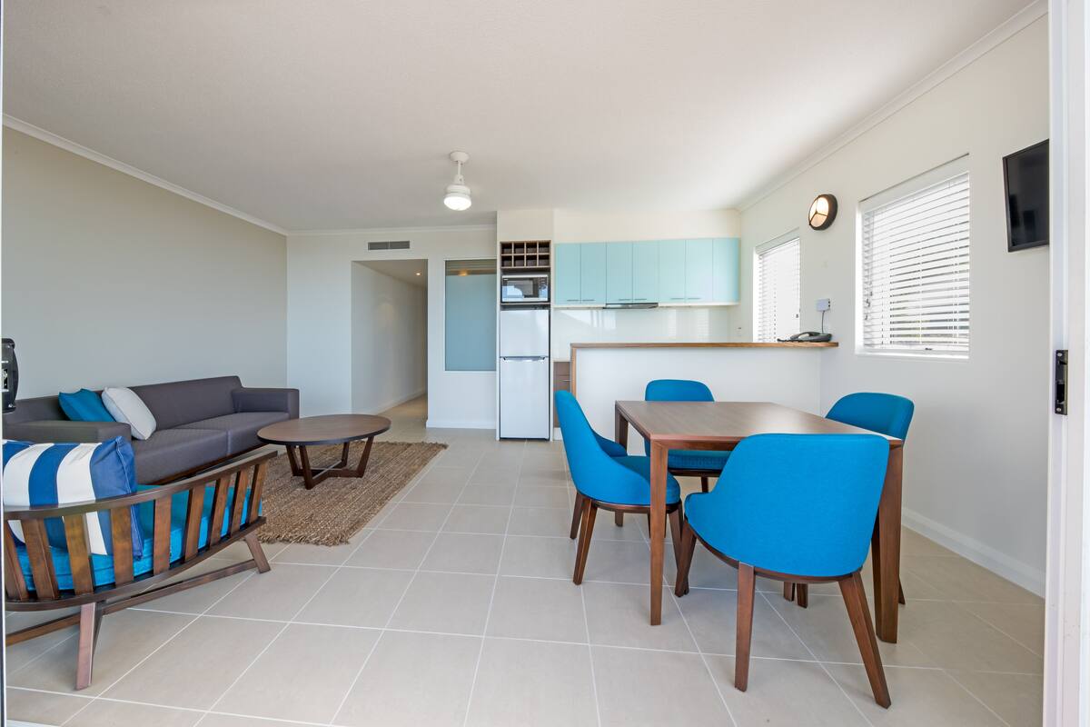 Un espacio habitable compacto con sofá, mesa de comedor, sillas, kitchenette y televisor montado en la pared.