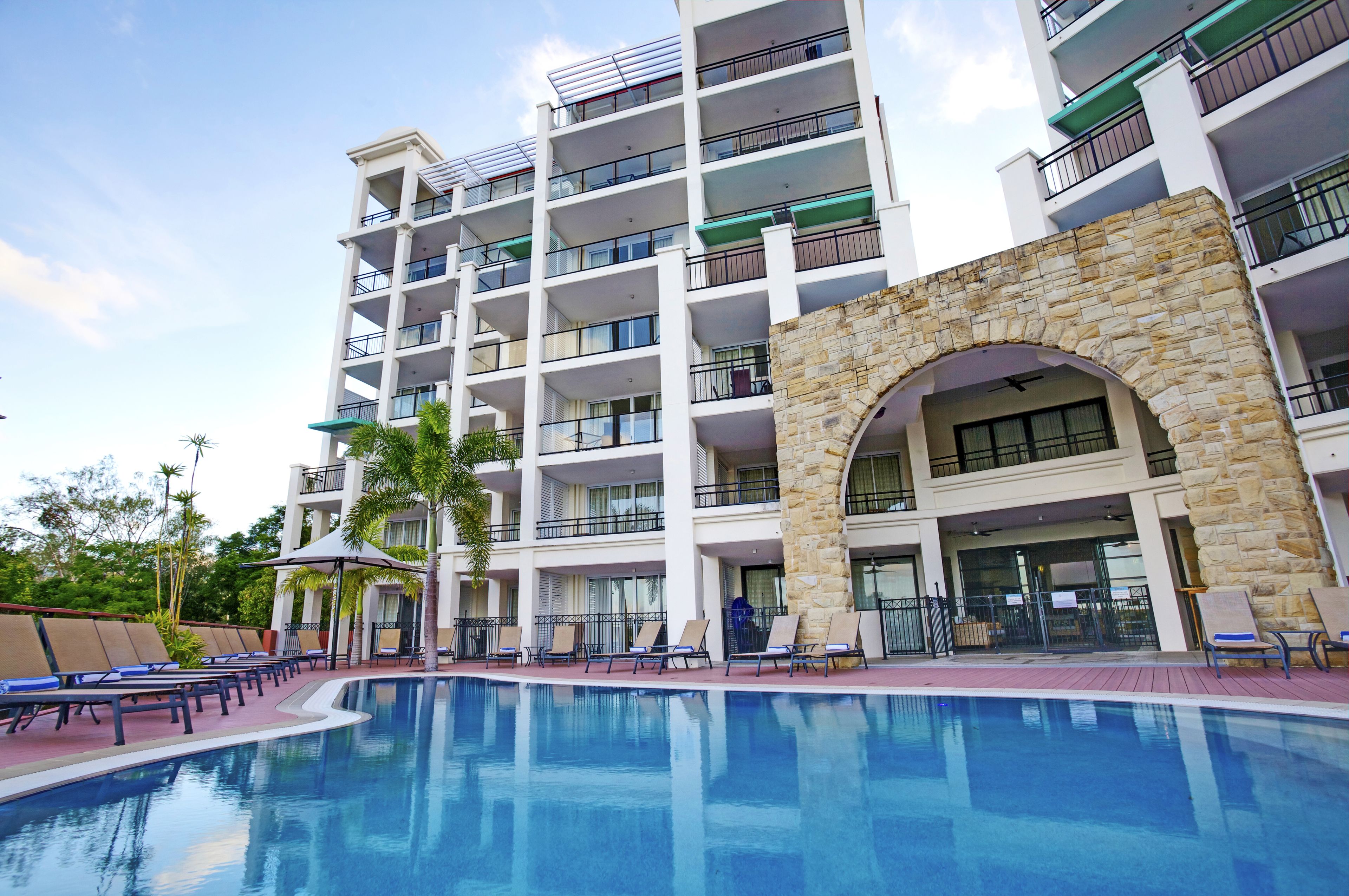 A multi-story hotel with a swimming pool, outdoor seating, and a stone archway.