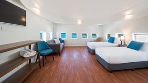 Habitación de hotel con dos camas, un sofá, un televisor y vistas al mar a través de las ventanas.