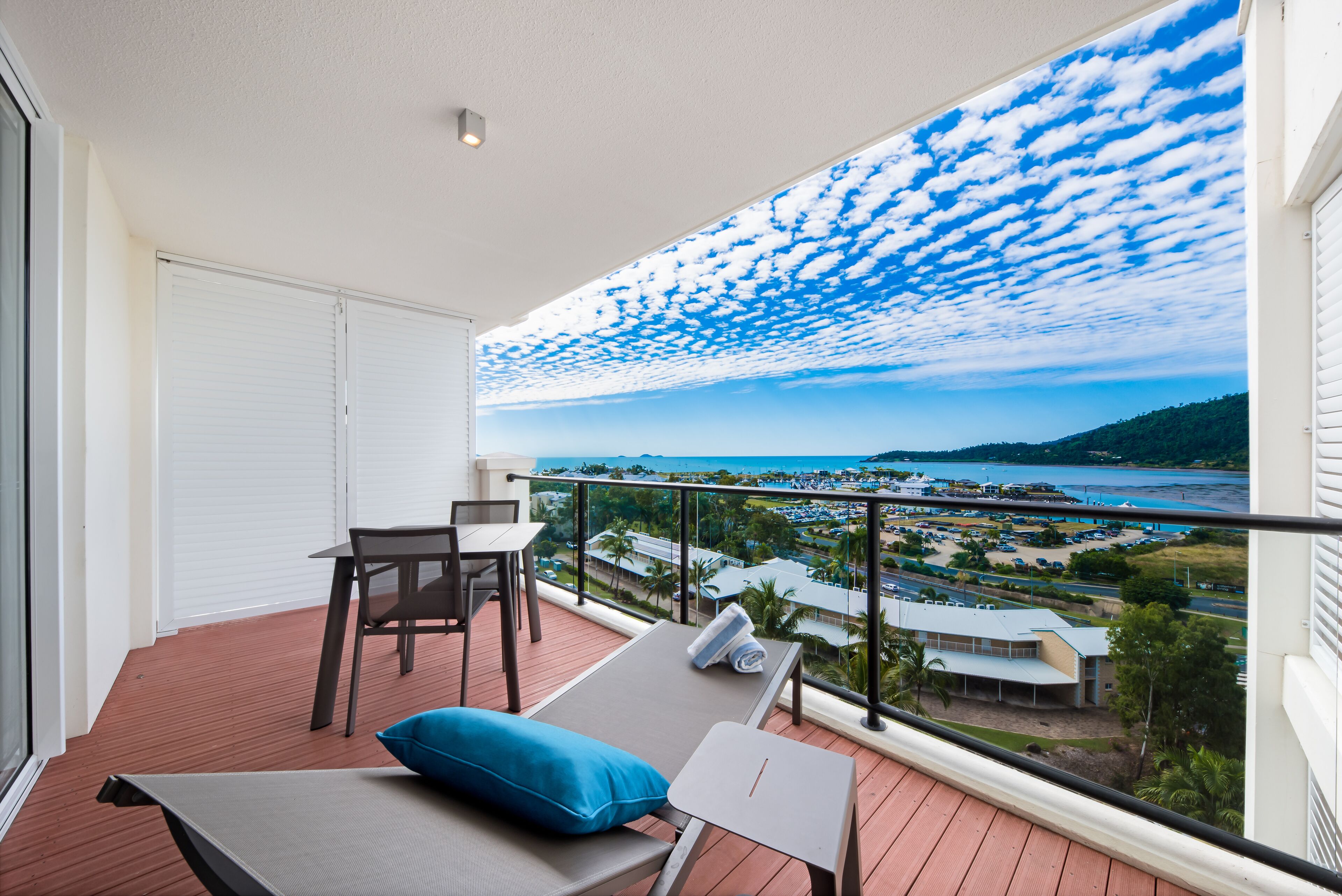 A balcony with a view of a beach and a resort area, including a pool and buildings.