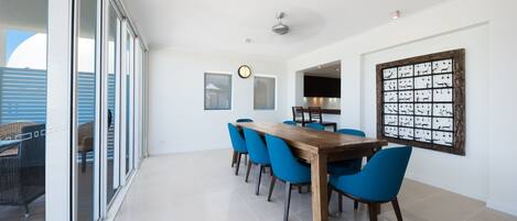 A dining area with a wooden table and blue chairs, large windows, and a decorative wall piece.