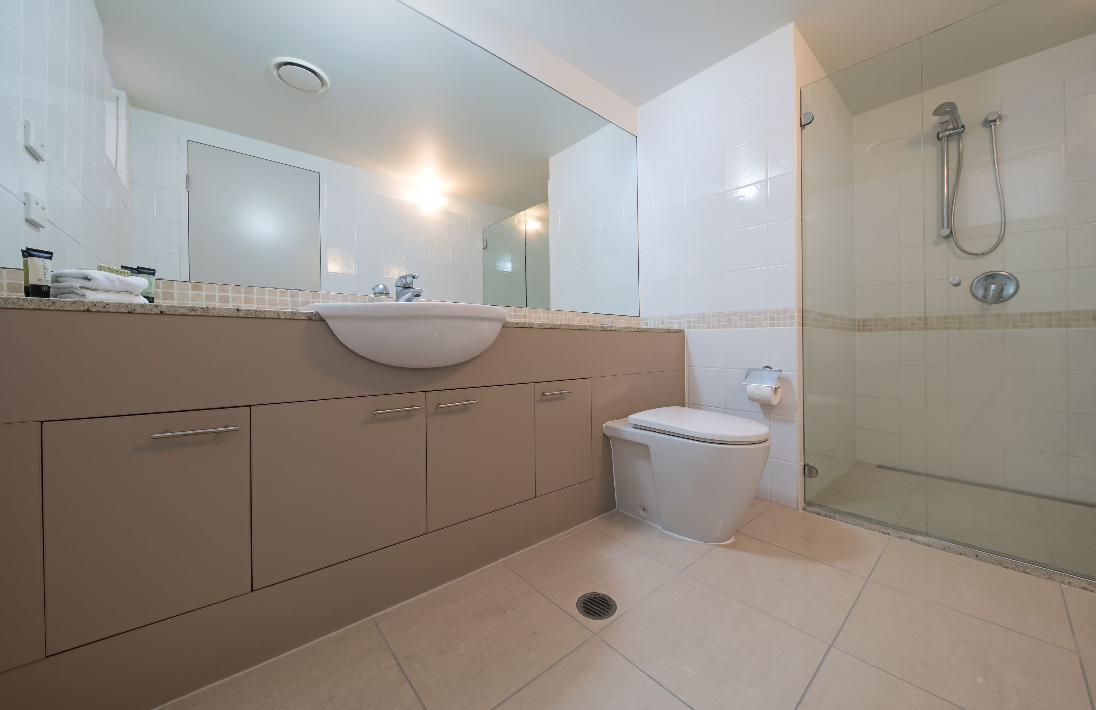 Een moderne badkamer met een wastafel, spiegel, toilet en douchecabine met glazen wanden.