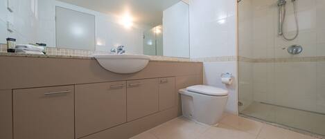 Un baño moderno con lavamanos, espejo, inodoro y ducha con mampara de vidrio.