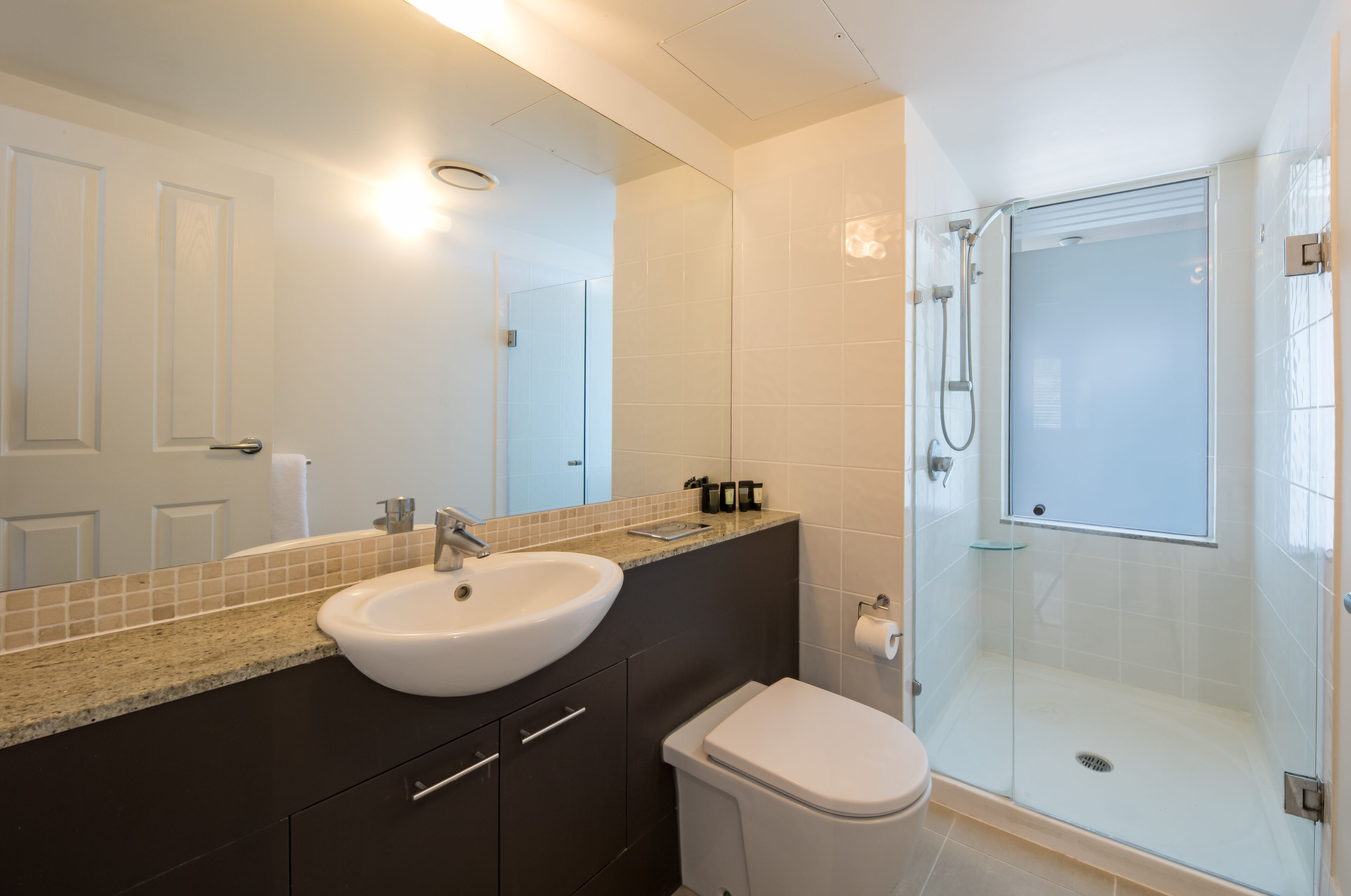 Une salle de bain moderne avec un lavabo blanc, des meubles sombres, une douche en verre et des toilettes.