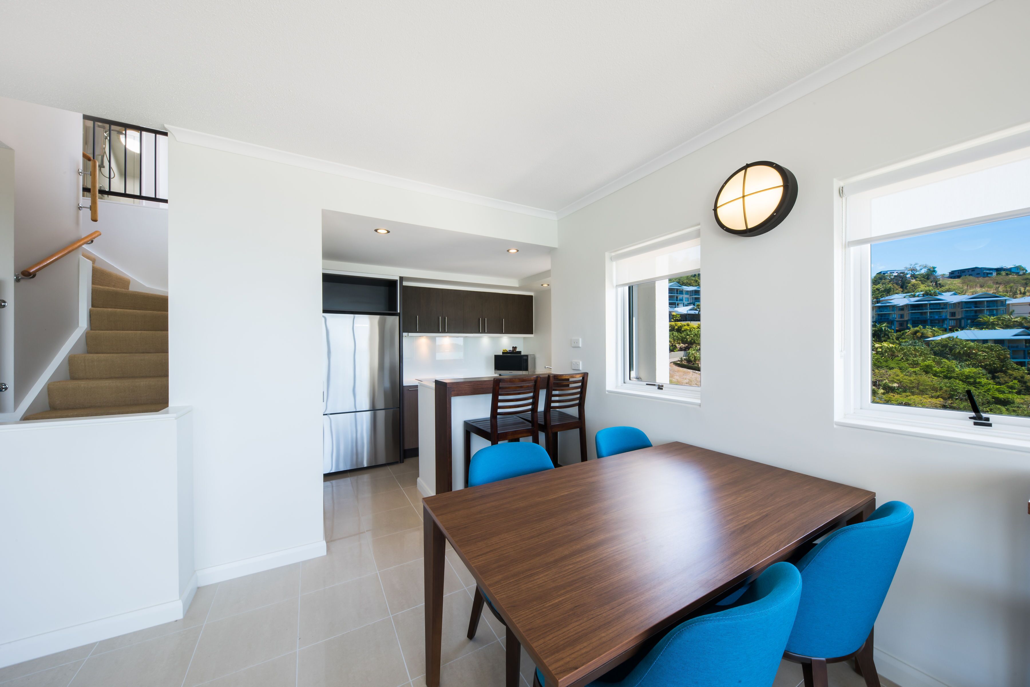 A modern kitchen with a dining area, a staircase, and a view of a residential area.