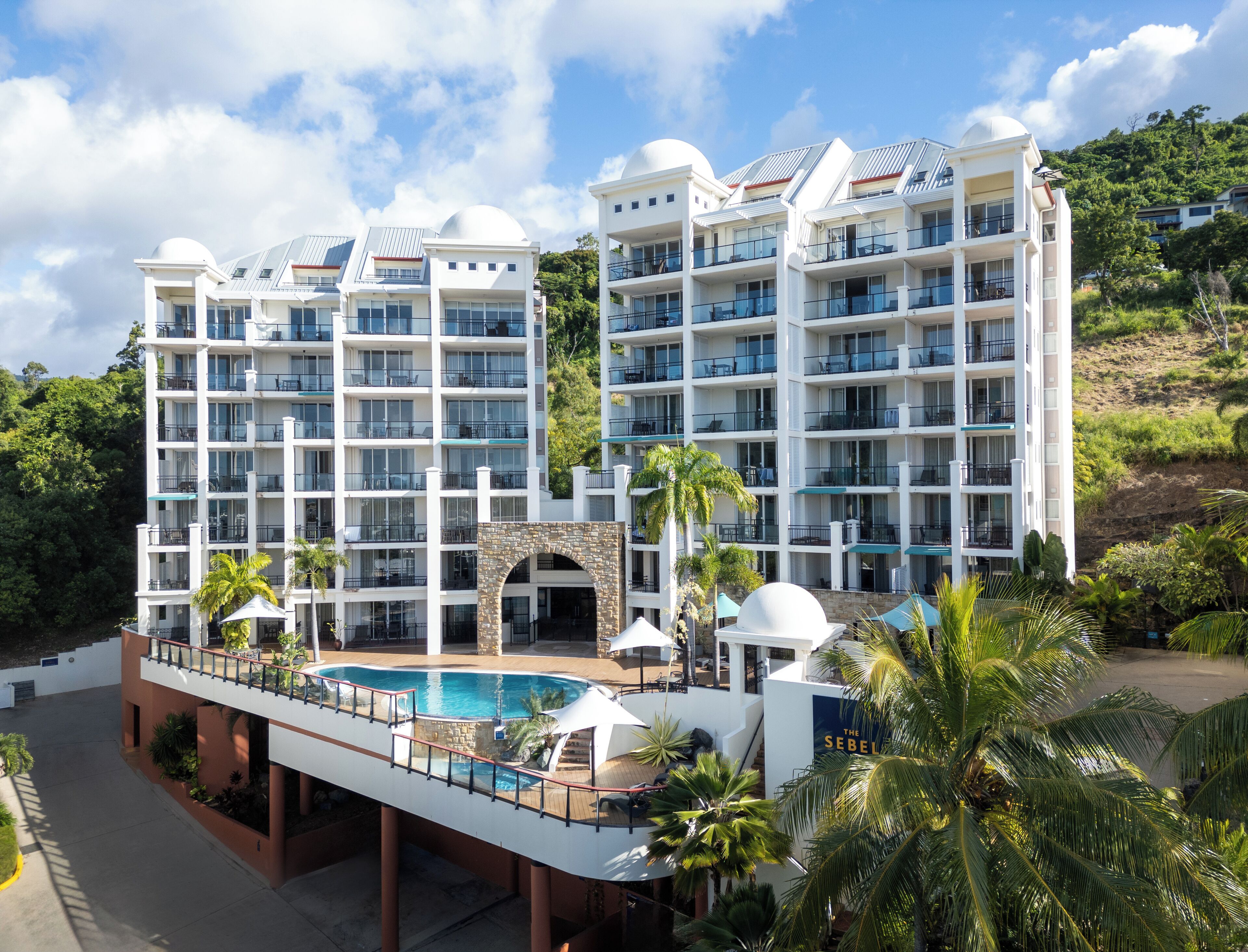 A multi-story hotel with balconies, a swimming pool, and lush greenery.