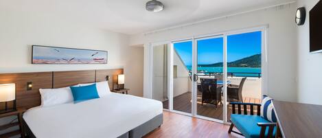Una habitación de hotel con una cama grande, un escritorio y un balcón con vistas al mar.