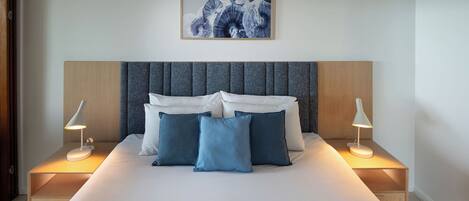 A neatly made bed with blue and white pillows, two bedside lamps, and a framed artwork above the bed.