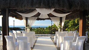 An outdoor wedding setup with white chairs and a draped canopy overlooking a scenic ocean view.