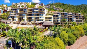 A multi-story hotel with balconies, a pool area, and lush greenery.